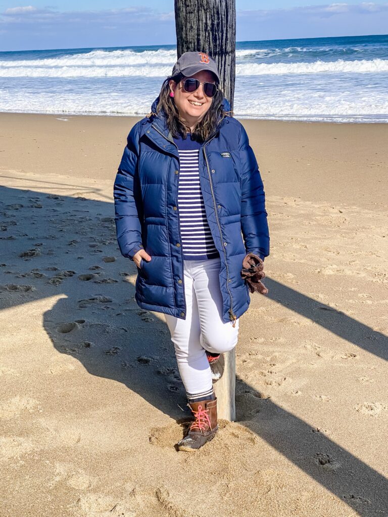 It Smells Like Snow The Perfect Women's Winter Coats. Nikki standing agents a piling wearing a blue winter coat with white jeans and a blue and white striped sweater with beaner boots.