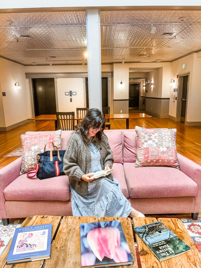 Nikki sitting on a pink couch reading a book